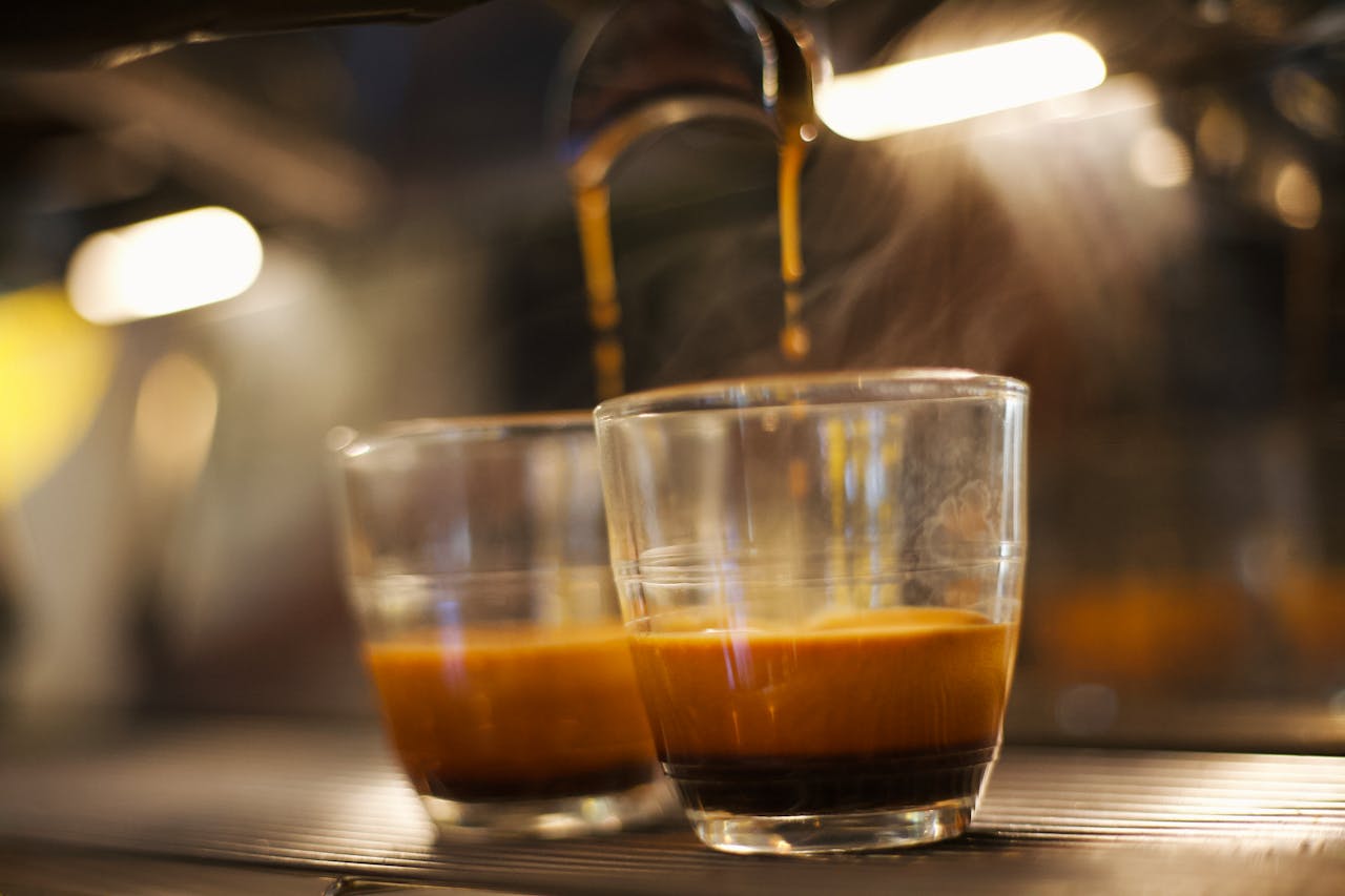 Close-up of espresso shot brewing in clear glass, showcasing coffee richness and steam.
